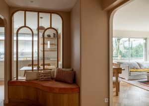 Alcôve avec banquette sur-mesure et verrière | HUGGY Coin banquette en bois et velours, surmonté d’une verrière à arcs arrondis donnant sur la cuisine, créant un espace convivial.